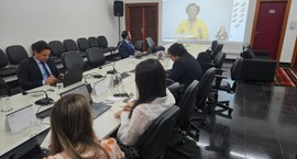 A imagem mostra um grupo de magistrados e magistradas reunidos em uma sala de reuniões, assistin...