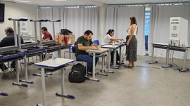 A imagem mostra uma seção de votação simulada, com cabinas de votação, mesas e equipamentos da J...
