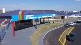 A imagem mostra a fachada de uma escola municipal, com estrutura ampla e moderna, identificada p...