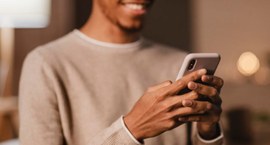 A imagem mostra um homem sorridente utilizando um smartphone, sugerindo operacionalizar o pagame...