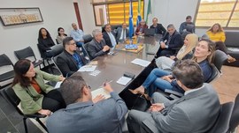 #PraTodosVerem - Uma sala de reuniões com cerca de 15 pessoas sentadas ao redor de uma mesa reta...