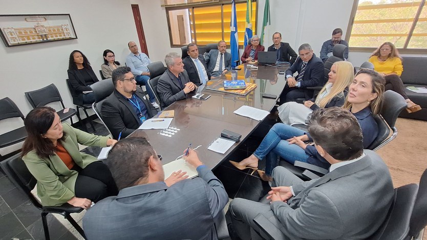 #PraTodosVerem - Uma sala de reuniões com cerca de 15 pessoas sentadas ao redor de uma mesa reta...