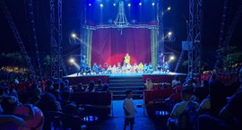 A imagem mostra o interior de um circo durante uma apresentação noturna. No picadeiro, diversas ...