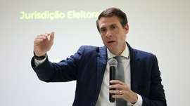 A imagem mostra o juiz Eduardo Calmon, um homem de terno azul, que segura um microfone enquanto ...