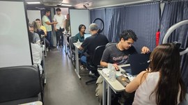 A imagem principal mostra o interior de uma unidade móvel de atendimento, com várias pessoas sen...