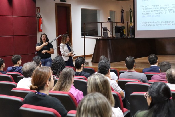 Foto em que aparecem os participantes, de costas, sentados nas cadeiras do Plenário. De frente p...