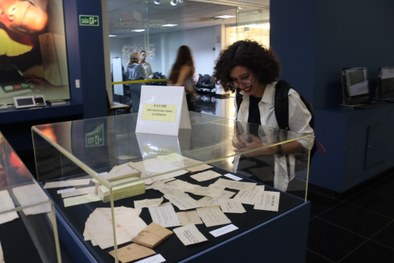 A imagem mostra uma estudante vendo os artefatos dentro do Memorial da Justiça Eleitoral