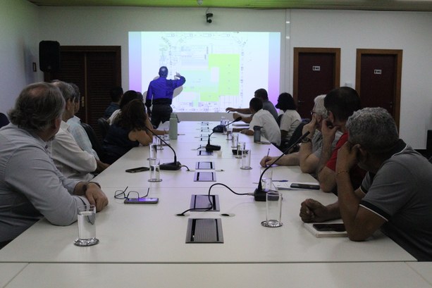 Saiba o que ocorre com os materiais de votação e urnas após o término das eleições #DescriçãodaImagem: Em uma mesa há treze pessoas sentadas olhando para a projeção de tela na par...