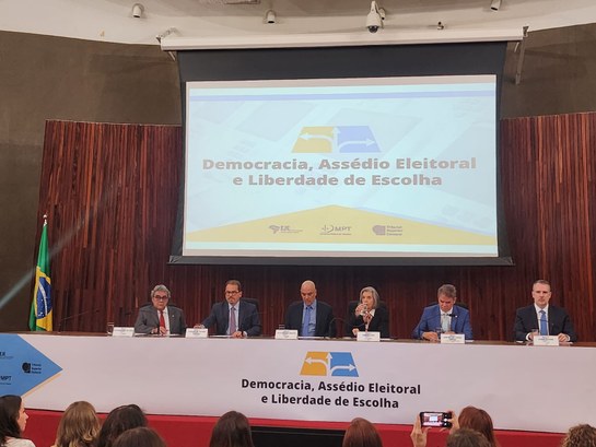 #DescriçãodaImagem: A imagem mostra a mesa de apresentação do evento , na mesa estão a ministra ...